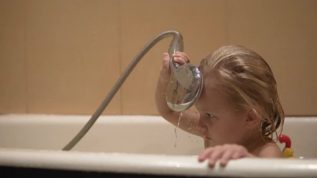 ittle girl washes in the bathroom. the child sits in the bathroom with water and tries to wash himself from the shower. Funny video.