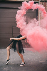 flexible young woman dancing in pink smoke on urban street