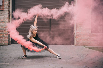young woman dancing in pink smoke on urban street