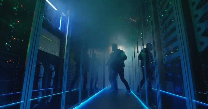 Wide, slow motion shot of a two hackers finishing hack and escaping a spark and smoke-filled corporate data center
