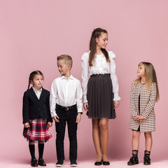 Obraz premium Cute smiling happy stylish children on pink background. Beautiful stylish teen girls and boy standing together and posing at studio. Classic style. Kids fashion and emotions concept.