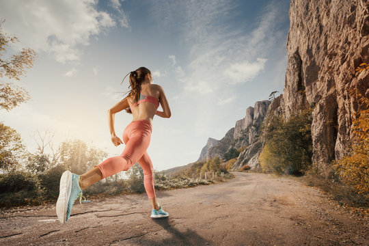 Young woman running on a mountain road in the beautiful nature. Girl runner in sneakers jogging workout outdoors. Weight loss concept. Healthy lifestyle.