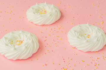 homemade white air meringues and confectionery decorations on pink background