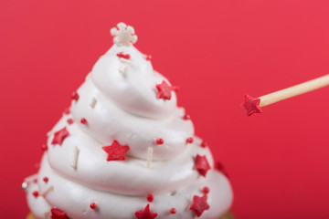on a red background stick with decoration in focus, next to a white cream cupcake in bokeh, holiday concept