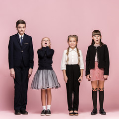 Cute smiling surprised stylish children on pink background. Beautiful stylish teen girls and boy standing together and posing at studio. Classic style. Kids fashion and emotions concept.