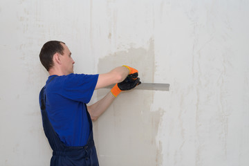a worker in blue workwear plasters and spats a wall in a living room