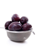 Steel colander with ripe plums isolated on a white background..