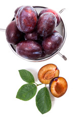 Steel colander with ripe plums, whole and half ripe plums with leaf isolated on a white background..