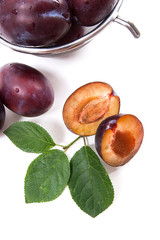 Steel colander with ripe plums, whole and half ripe plums with leaf isolated on a white background..
