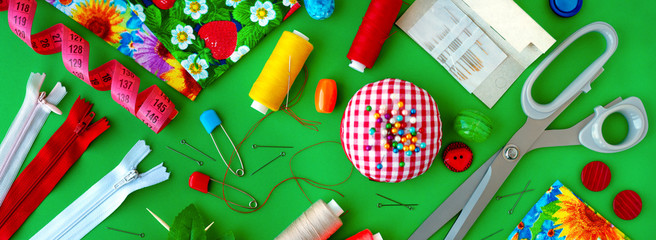 Panorama of items for sewing on a green background. Bright panorama is visible from above. Fabric, tailoring scissors, measuring tape, needles, threads and buttons for sewing clothes.