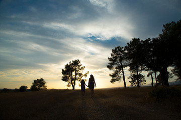 Backlight of a mother and daughter in a pine forest with yellow sky sunrise and sunset