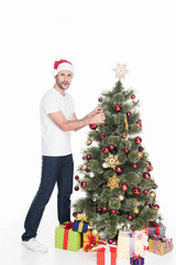 young man in red santa claus hat decorating christmas tree isolated on white