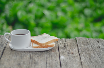 White bread and glass placed on the table in the morning.On the breakfast table there was a glass of coffee and a plate of bread.