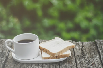 White bread and glass placed on the table in the morning.On the breakfast table there was a glass of coffee and a plate of bread.
