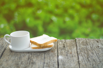 White bread and glass placed on the table in the morning.On the breakfast table there was a glass of coffee and a plate of bread.Breakfast set on wooden floor in the morning.