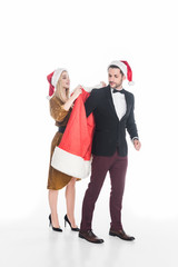 young woman putting santa claus costume on boyfriend isolated on white