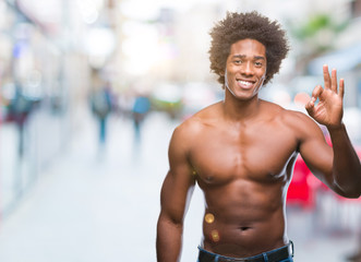 Fototapeta na wymiar Afro american shirtless man showing nude body over isolated background smiling positive doing ok sign with hand and fingers. Successful expression.