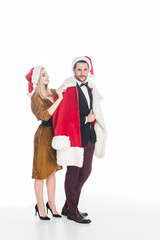 young woman putting santa claus costume on boyfriend isolated on white