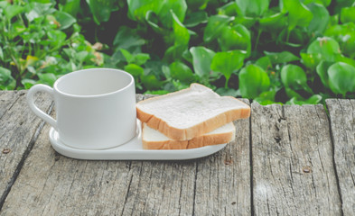 White bread and glass placed on the table in the morning.On the breakfast table there was a glass of coffee and a plate of bread.Breakfast set on wooden floor in the morning.