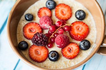 oatmeal porridge in ceramic bowl with fresh ripe berries over blue wooden background