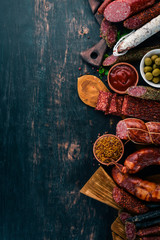 Assortment of salami and snacks. Sausage Fouet, sausages, salami, paperoni. On a black wooden background. Top view. Free space for your text.