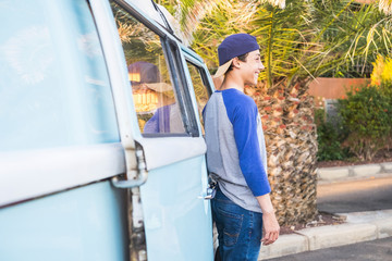 Young teenager standing near an old vintage bus in tropical place. Surfer lifestyle and beautiful young people smiling and enjoying life. Millennial alternative concept