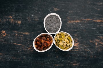 Raisins, sunflower seeds and poppy seeds. On a black wooden background. Top view. Free copy space.