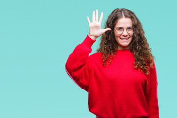 Beautiful brunette curly hair young girl wearing glasses and winter sweater over isolated background showing and pointing up with fingers number five while smiling confident and happy.