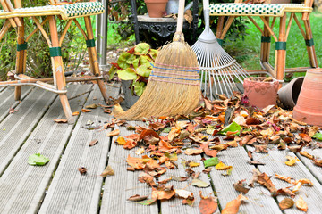 broom and rake in leaves on wooden terrace 