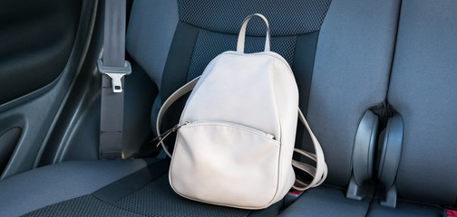Beige leather backpack on a grey backseat of a car.