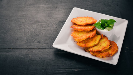 Potato cakes with sour cream. Potato pancakes. Ukrainian cuisine. On the old wooden background. Free space for text. Top view.