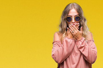 Beautiful young blonde woman wearing retro sunglasses over isolated background shocked covering mouth with hands for mistake. Secret concept.