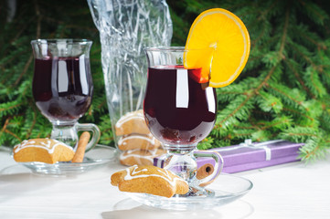 Mulled wine with cinnamon sticks in glass and cookies on the wooden table with christmas tree branch on background