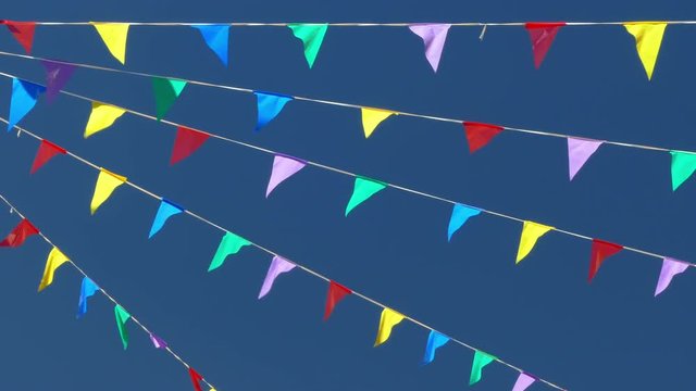 Multi colored flags on the blue sky.
Pennants moved for the wind, symbol of celebration and fun.