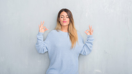 Young adult woman over grey grunge wall wearing winter outfit relax and smiling with eyes closed doing meditation gesture with fingers. Yoga concept.