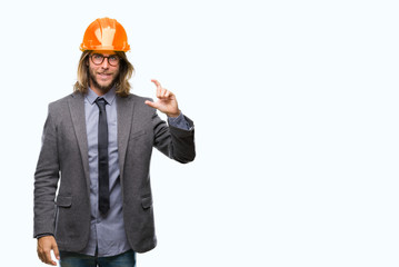 Young handsome architec man with long hair wearing safety helmet over isolated background smiling and confident gesturing with hand doing size sign with fingers while looking and the camera