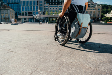 cropped image of man using wheelchair with bag in city