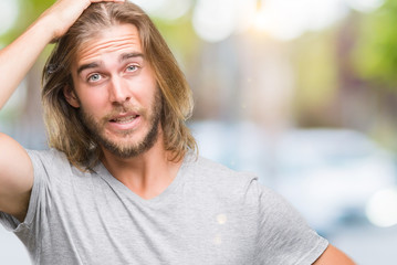 Young handsome man with long hair over isolated background holding football ball stressed with hand on head, shocked with shame and surprise face, angry and frustrated. Fear and upset for mistake.