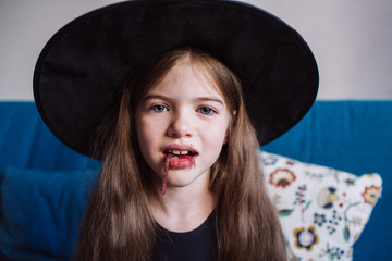 a girl in a witch suit and a black hat eating jelly worms at a celebration of Halloween