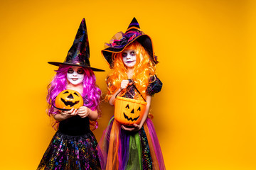 Two Beautiful girls in a witch costumes and hats on a yellow background scaring and making faces....