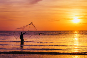 Silhouette of fisherman throwing fishing net in morning at tropical sea at beautiful sunrise,...