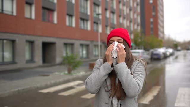 Young female sick woman, girl blowing nose to paper napkin and sneezing at street outside. healthcare, flu, people, health, disease, pain, autumn, winter, crunny nose, flu virus epidemic concept slow