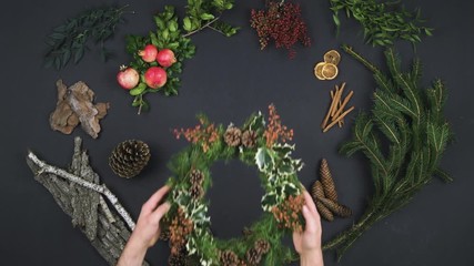 Overhead person hands putting wreath garland on text copy space.Vertical top view of dark table with natural leaves,pine cones,bark, pomegranate.Xmas holiday season social card background.4k video - Powered by Adobe