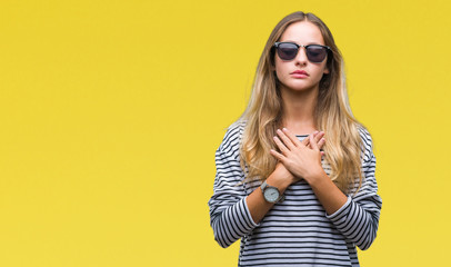 Fototapeta premium Young beautiful blonde woman wearing sunglasses over isolated background smiling with hands on chest with closed eyes and grateful gesture on face. Health concept.