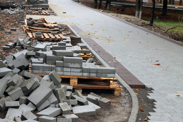 A craftsman in gloves with a rubber mallet lays concrete blocks on a gravelly sand base. Laying...