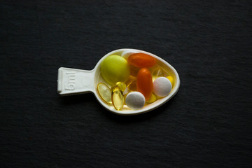 Pills in white measuring spoon on dark background.