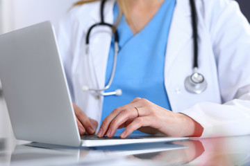 Doctor typing on laptop computer while sitting at the glass desk in hospital office. Physician at work. Medicine and healthcare concept