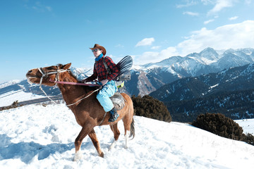 A man in a cowboy hat riding a horse in the snow. Winter. the mountains.