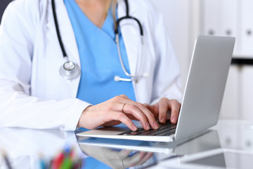 Doctor typing on laptop computer while sitting at the glass desk in hospital office. Physician at work. Medicine and healthcare concept