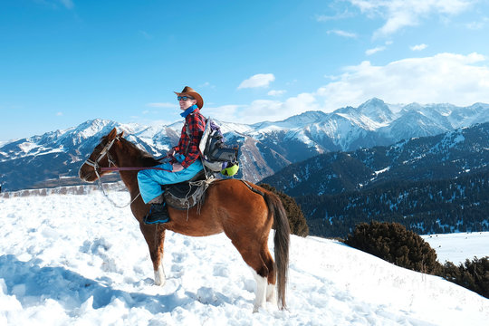 Freeride On Horseback. A Man In A Cowboy Hat Riding A Horse In The Snow. Winter. The Mountains.